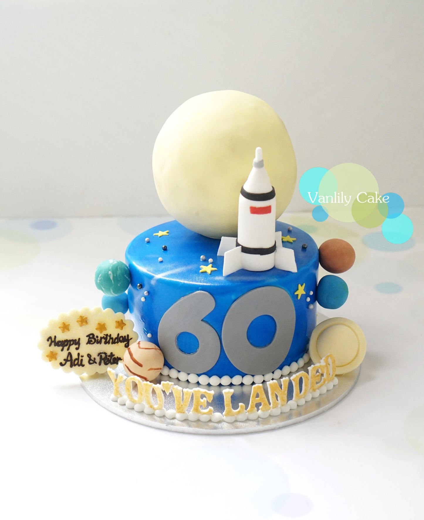 Vanlily Cake 宇航員太空主題一歲生日蛋糕，帶有立體航天員模型、灰色月亮、金色星球、火箭裝飾及客製化金色英文名字 ANSON。