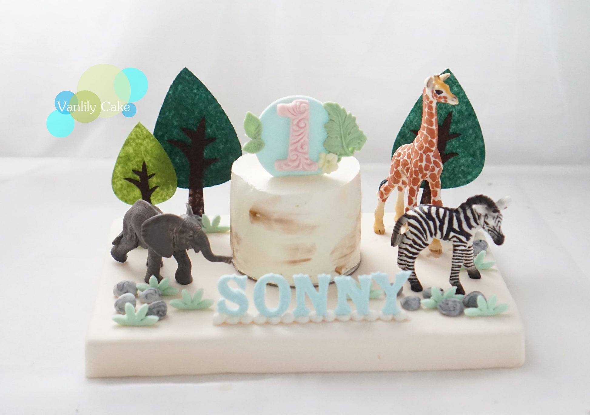  Vanlily Cake 3 吋森林主題一歲生日蛋糕，白色蛋糕體配上大象、長頸鹿與斑馬模型，前方有藍色客製化姓名「SONNY」，適合低敏或小家庭慶祝。