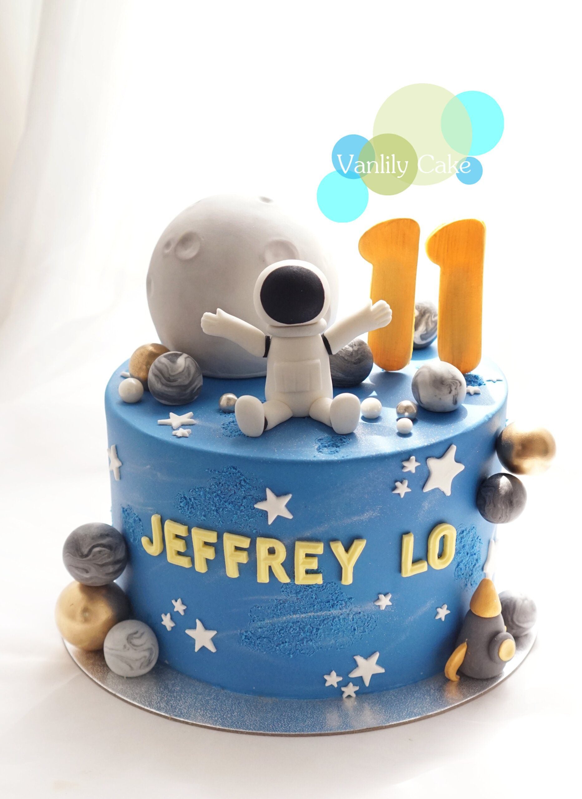 Vanlily Cake 宇航員太空主題一歲生日蛋糕，帶有立體航天員模型、灰色月亮、金色星球、火箭裝飾及客製化金色英文名字 ANSON。