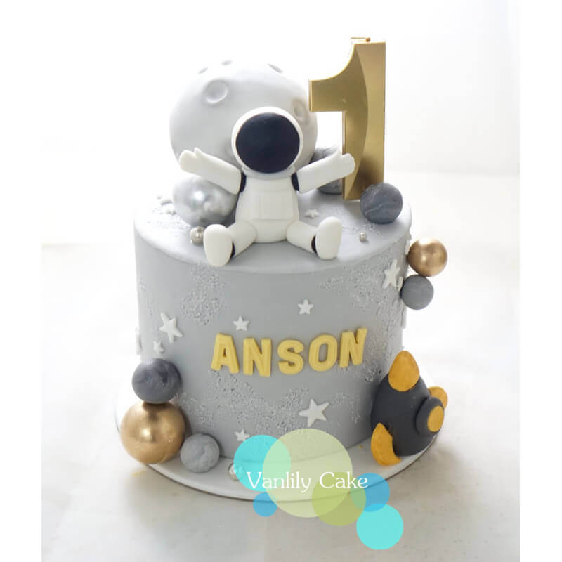 Vanlily Cake 宇航員太空主題一歲生日蛋糕，帶有立體航天員模型、灰色月亮、金色星球、火箭裝飾及客製化金色英文名字 ANSON。