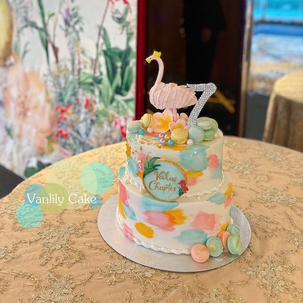 Vanlily Cake 雙層火烈鳥Flamingo主題造型蛋糕，白色基底飾有繽紛手繪彩塊，頂端裝飾立體粉紅火烈鳥、繽紛馬卡龍與閃亮數字，充滿藝術氣息。