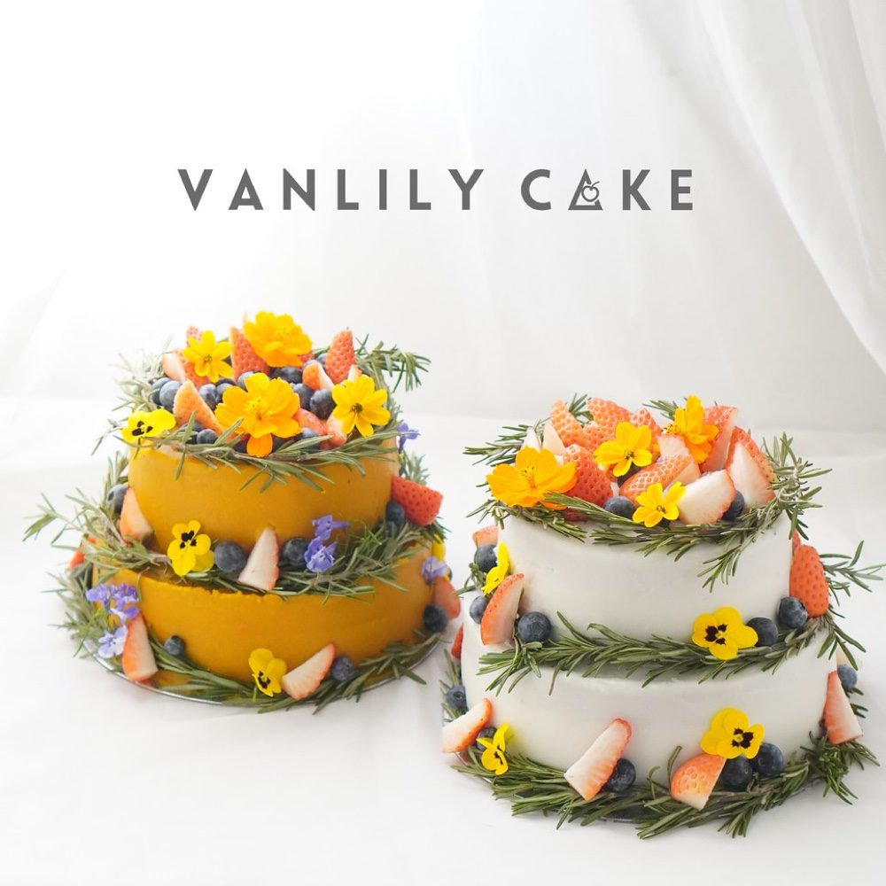 Vanlily Cake 純素香蕉生日蛋糕，展示淮山（白色外層）與蕃薯南瓜（黃色外層）兩款選擇，裝飾有新鮮水果、藍莓與迷迭香，適合一歲寶寶、素食與過敏人士。