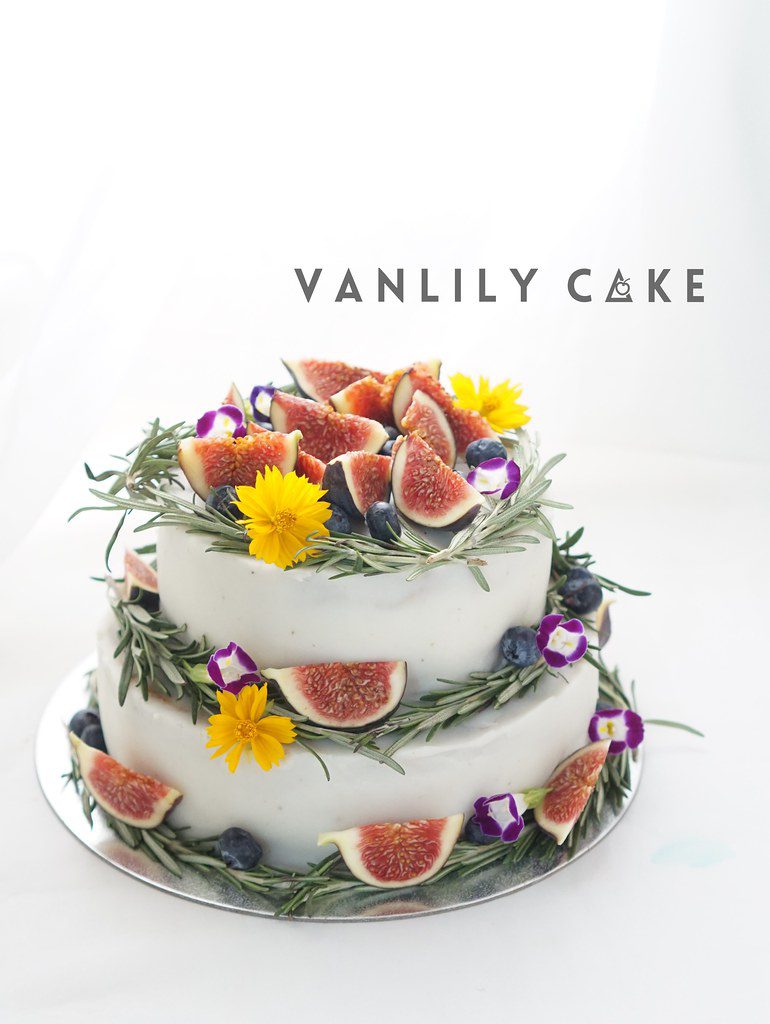Vanlily Cake 純素香蕉生日蛋糕，展示淮山（白色外層）與蕃薯南瓜（黃色外層）兩款選擇，裝飾有新鮮水果、藍莓與迷迭香，適合一歲寶寶、素食與過敏人士。